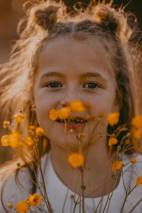 Meisje met gele bloemetjes in het gras op het gouden uur