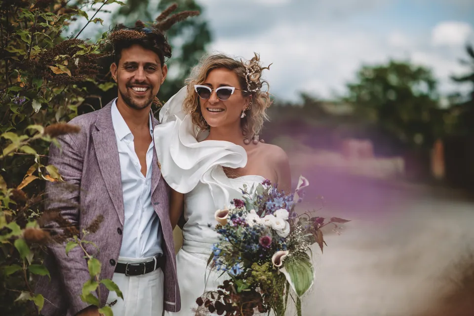 Bruidspaar met bloemen poseert lachend voor de camera