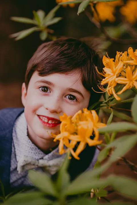 Communicant tussen oranje azalea's kijkt lachend in de lens