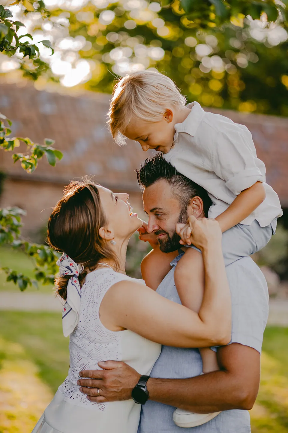 Ouders kussen in de tuin, met hun zoontje op papa's schouders