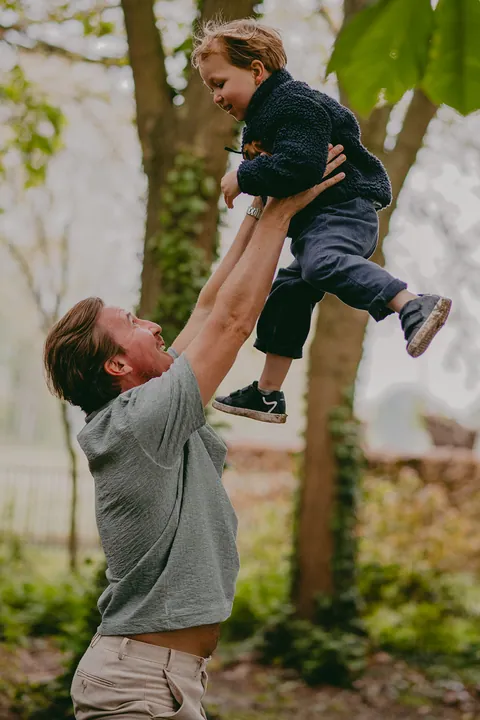 Papa gooit zijn zoontje hoog in de lucht in het voorjaarsbos