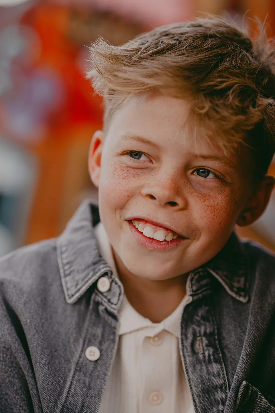 Jongen in spijkerjasje lacht voor een kleurrijke graffitimuur