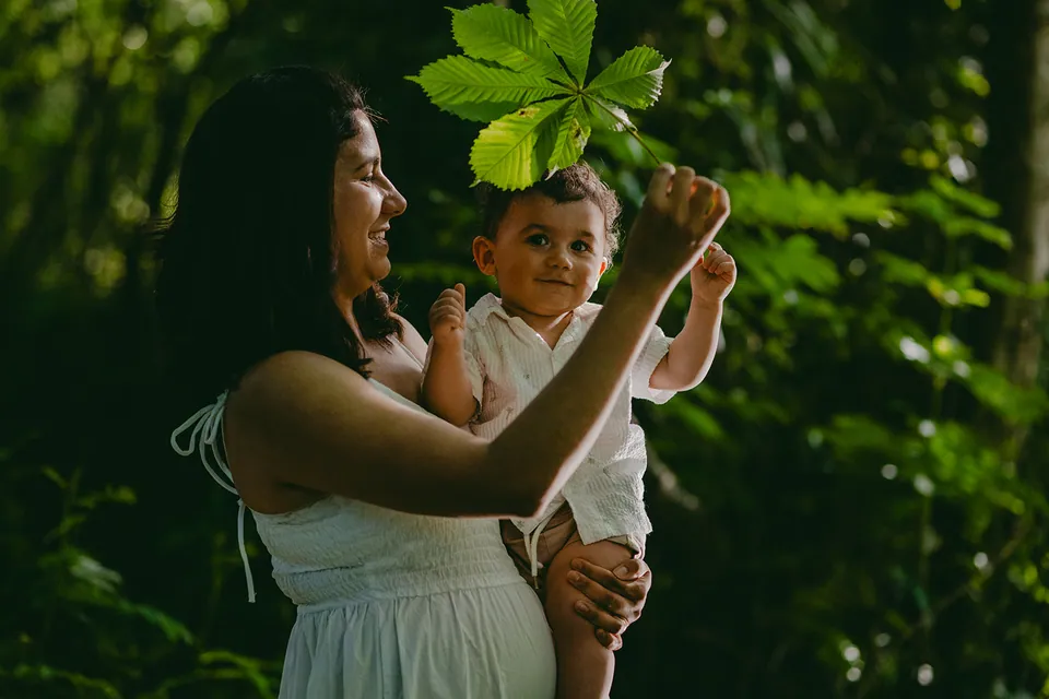 Mama houdt haar baby op, die naar een groot blad grijpt