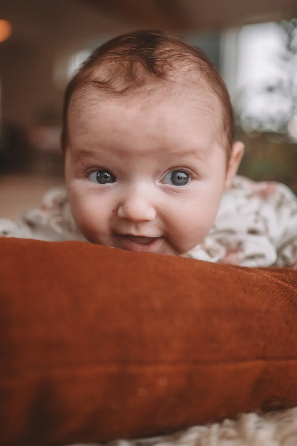 Baby gluurt over een roestbruin kussen