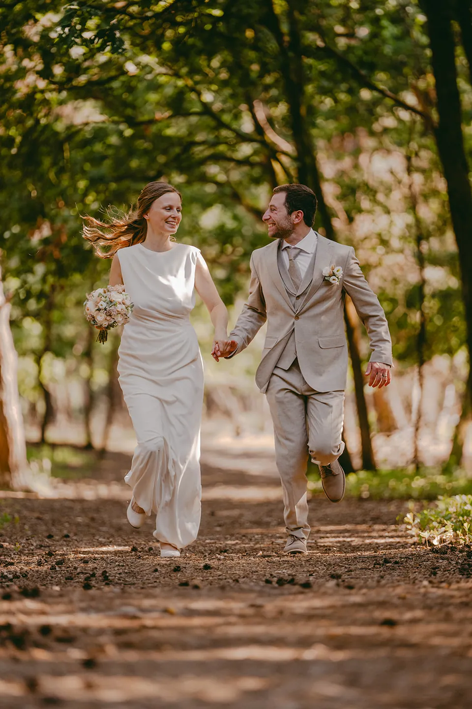 Bruidspaar loopt hand in hand lachend door het bos